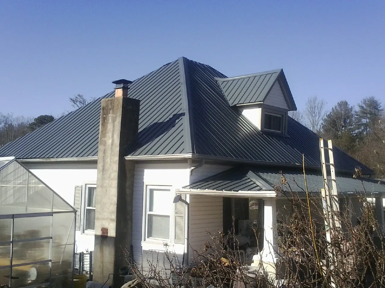 Dark blue standing seam metal roof on a white farmhouse with dormer — Slate & Tile Roof Repair by Roofing Brothers in Tobaccoville