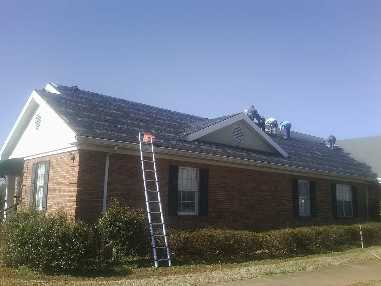 Crew tearing shingles off a brick ranch roof with a ladder set — Emergency Roof Repair work by our crew in Tobaccoville