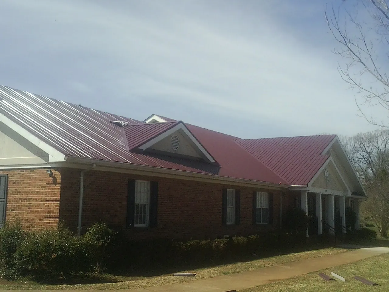 Red metal roof with gabled entries on a long brick building, from a Hail Damage Roof Repair job in Tobaccoville