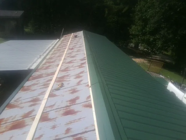 Old rusted panels beside newly installed green metal roofing — Wind Damage Roof Repair by Roofing Brothers in Tobaccoville
