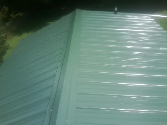 New green metal panels meeting at the ridge of a roof — Flat Roof Repair work by our crew in Tobaccoville