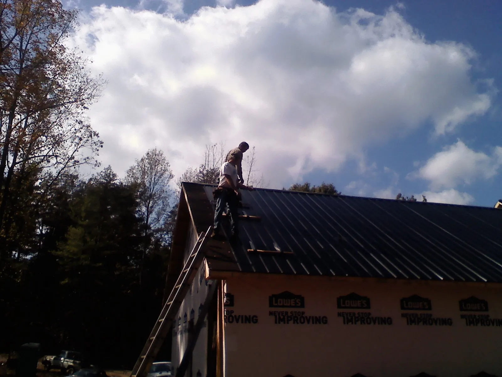 Roofer fastening dark metal panels high against a cloudy sky, from a Roof Inspection job in Tobaccoville