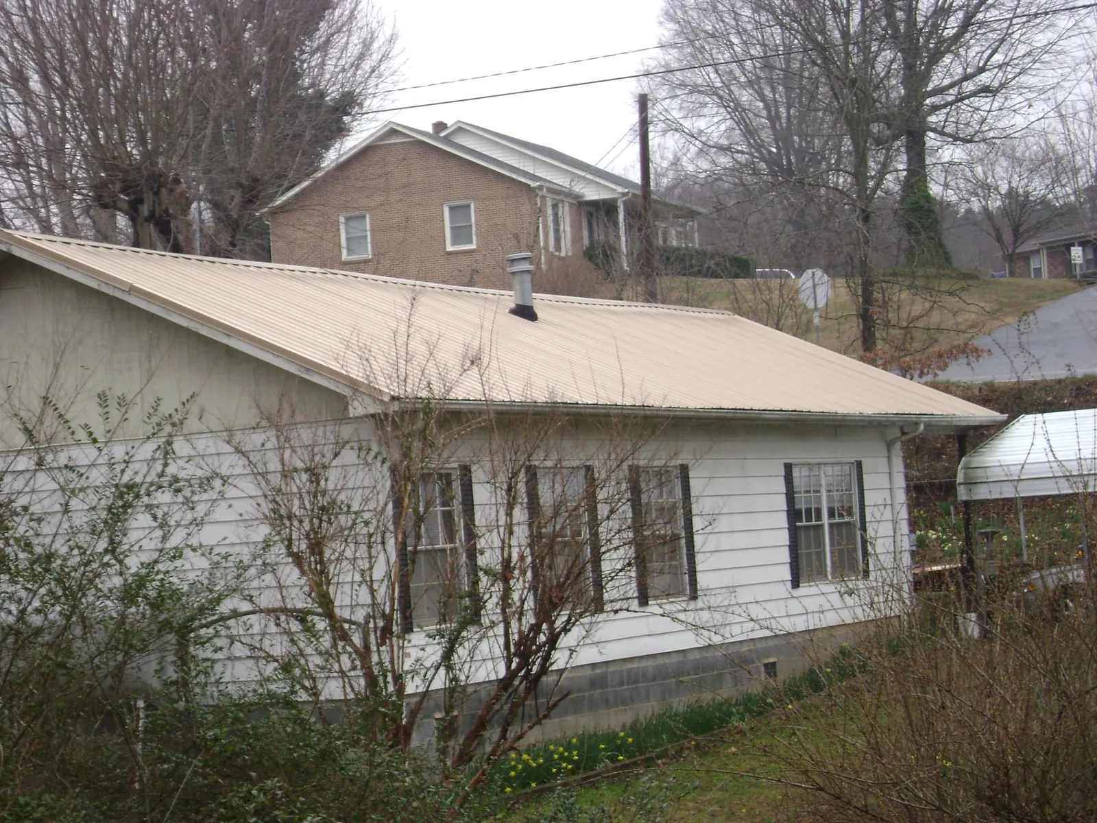 Tan metal roof on a white sided house set into a hillside — Commercial Roofing by Roofing Brothers in Tobaccoville